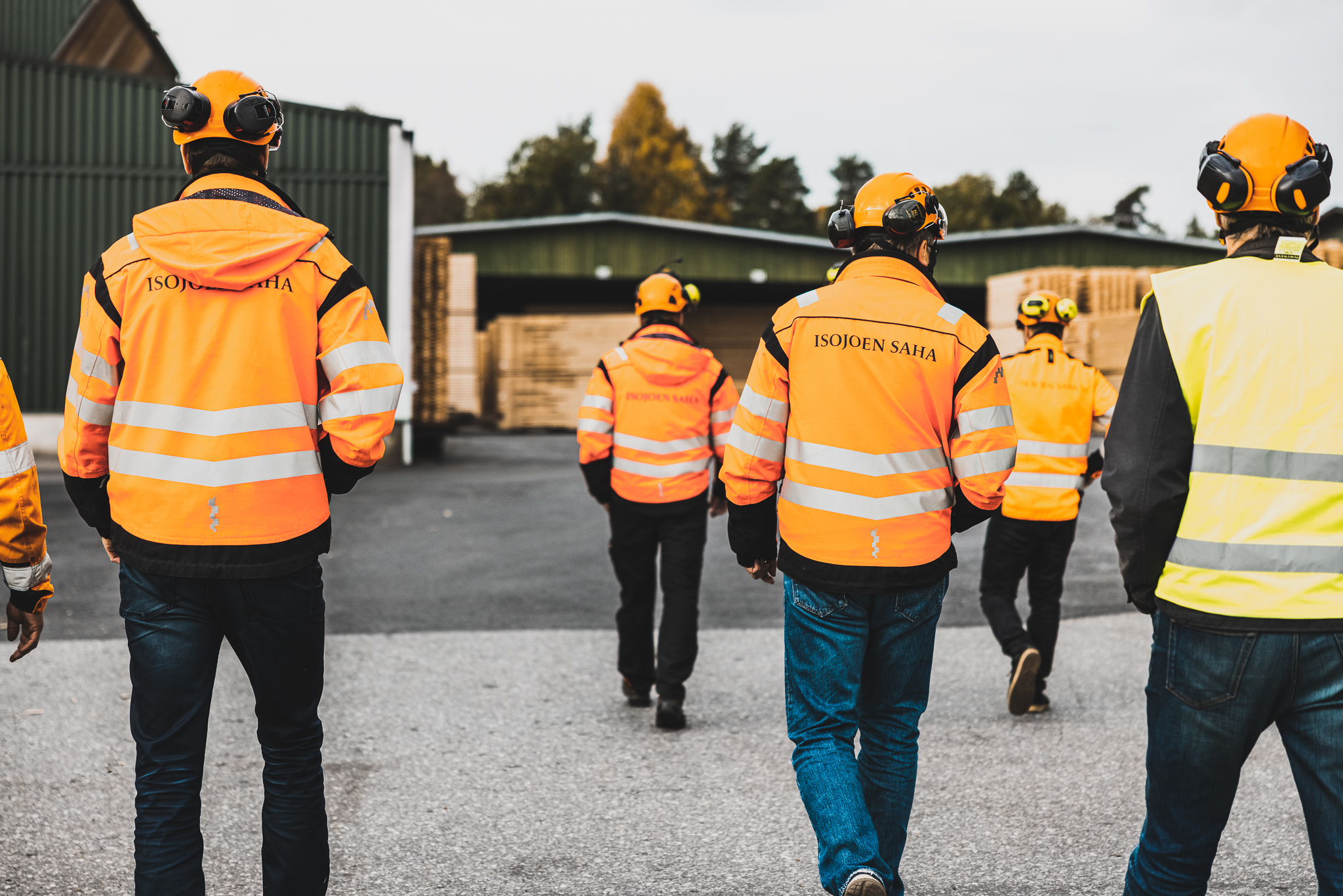 Isojoen Sahan työntekijöitä kulkevat kamerasta poispäin, kaikilla on oranssit Sahan takit ja kypärät.